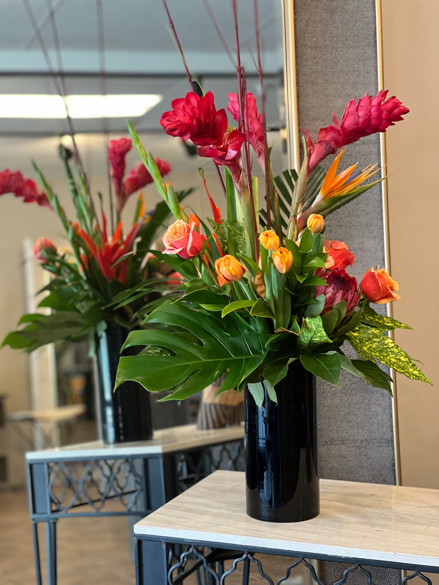 Tropical design with clustered, spilling foliage, black cylinder vase