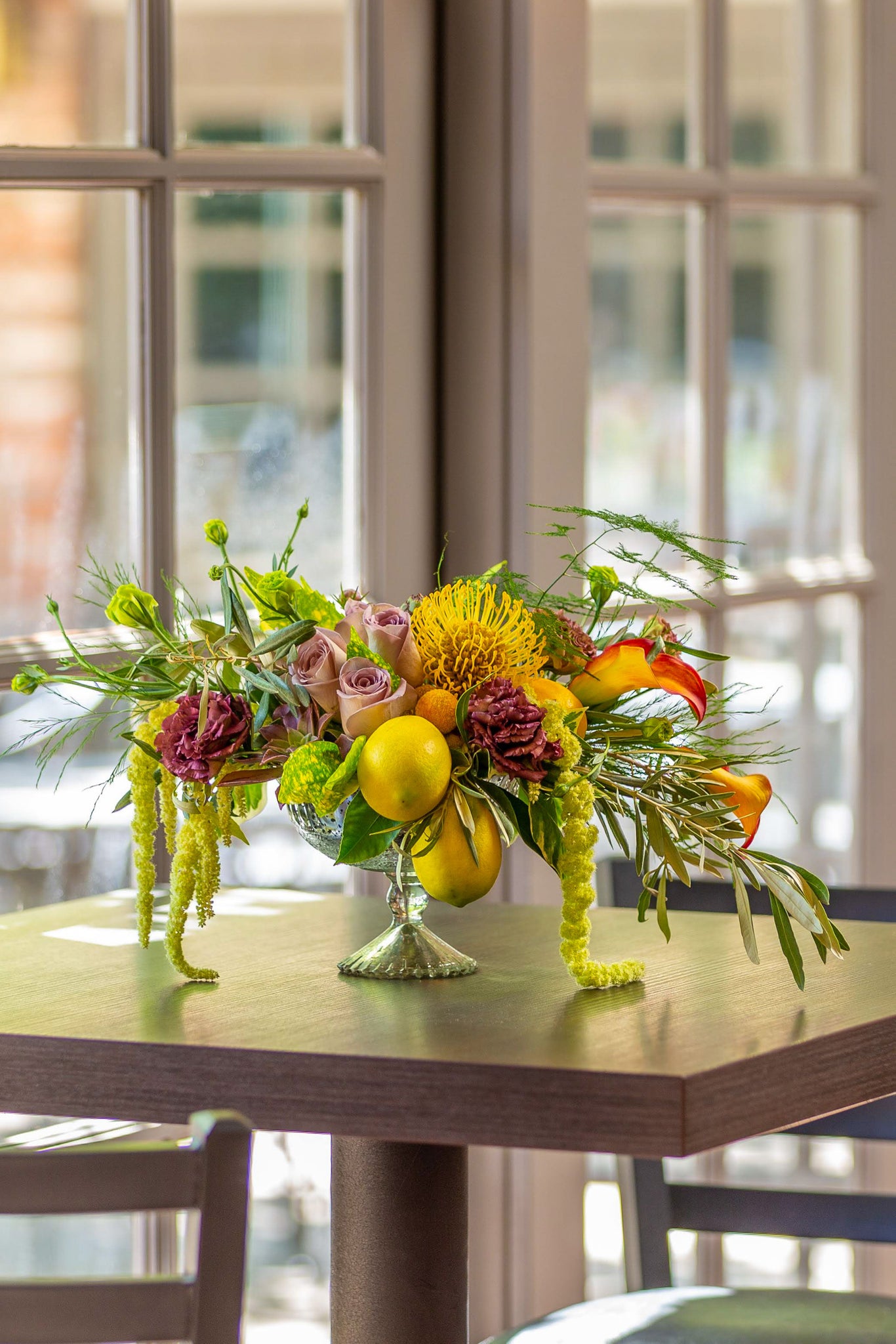 Lush mix with fruit, draping foliage, glass urn